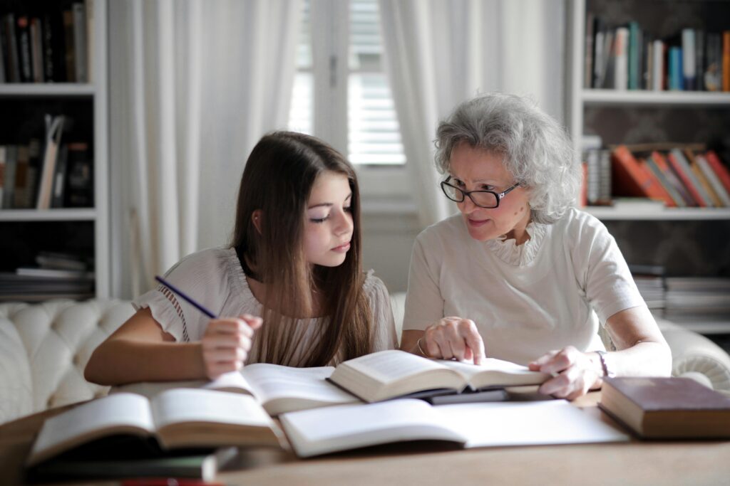 pexels-photo-3768129-3768129 A grandmother helps her teenage granddaughter with homework, surrounded by books indoors.